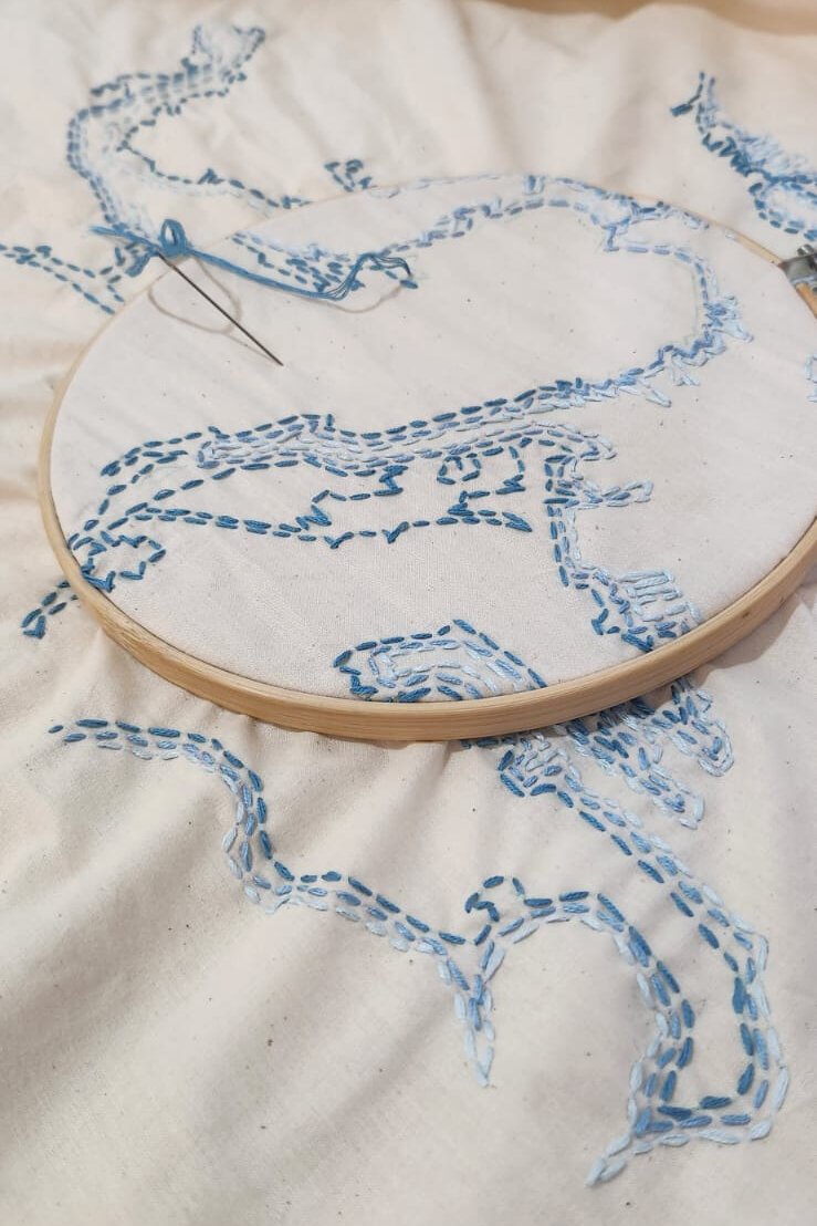 Embroidery hoop with needle and blue thread mid-stitch on the Boston map